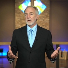 Click to show details - Rev. Neusom Holmes | Senior Minister Neusom Holmes wearing black suit, light blue shirt and tie in sanctuary delivering a sermon