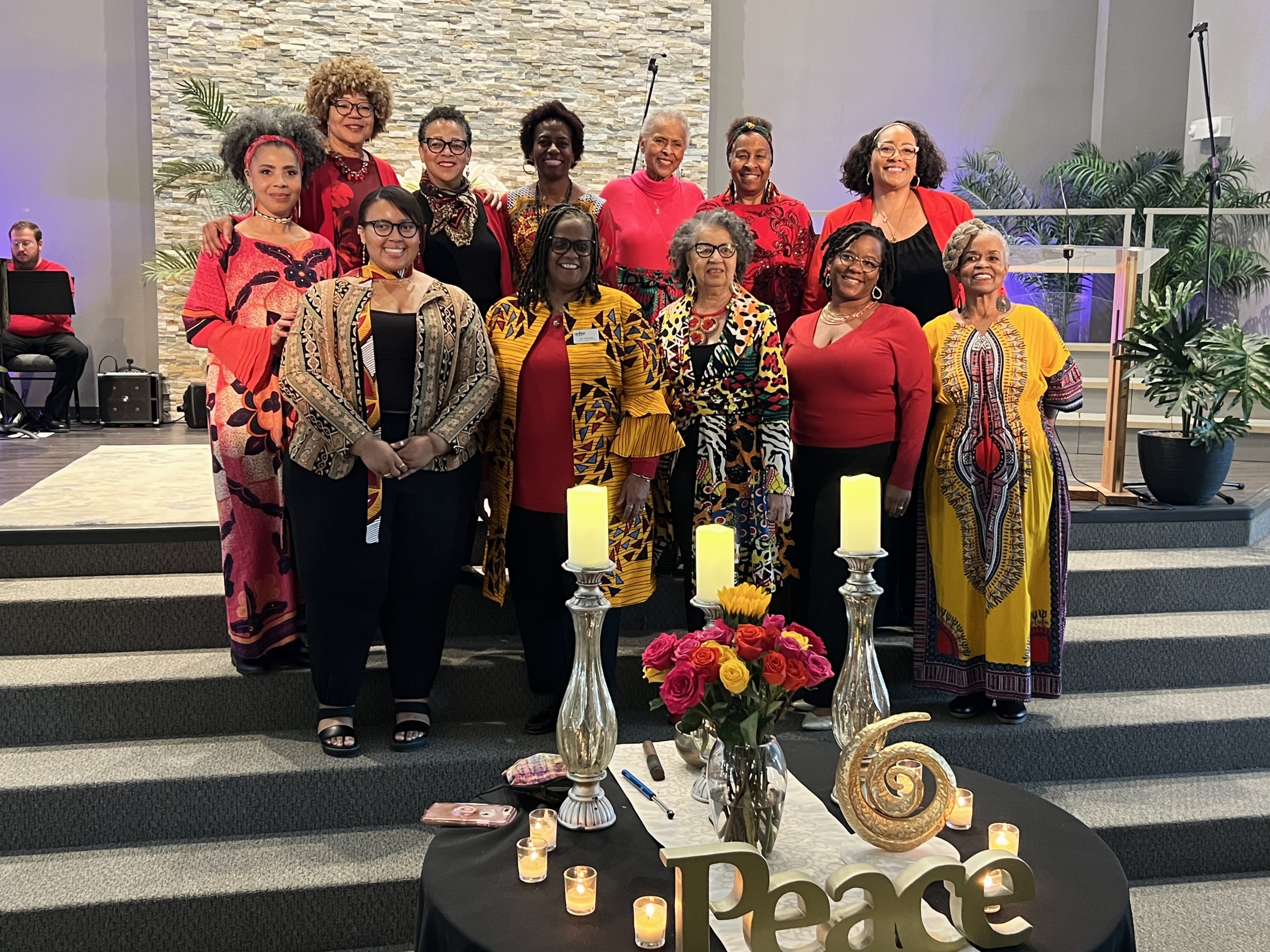 Group of twelve Black women dressed in bright yellow, red, black, orange clothing representing traditional dress of the culture.