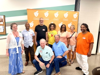 Diverse group of nine people in front of Oak City Cares banner