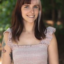 Tia Redman standing outside, smiling at camera wearing light colored horizontal striped, ruffled cap sleeve dress.