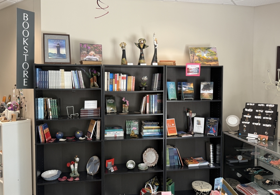 Image of The Higher Shelf bookstore and gift shop at Unity of the Triangle, 5570 Munford Road, Raleigh NC. Books, ceramics, jewelry, posters displayed on black shelving.