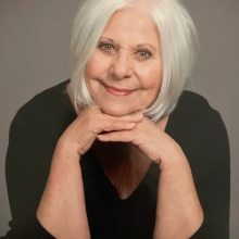 SandyRifkinbiopic Sandy Rifkin posed with chin resting on linked hands, wearing black blouse