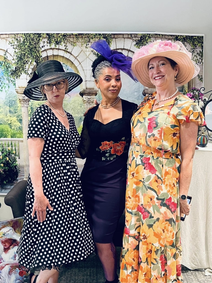three diverse ladies wearing garden party hats and dresses